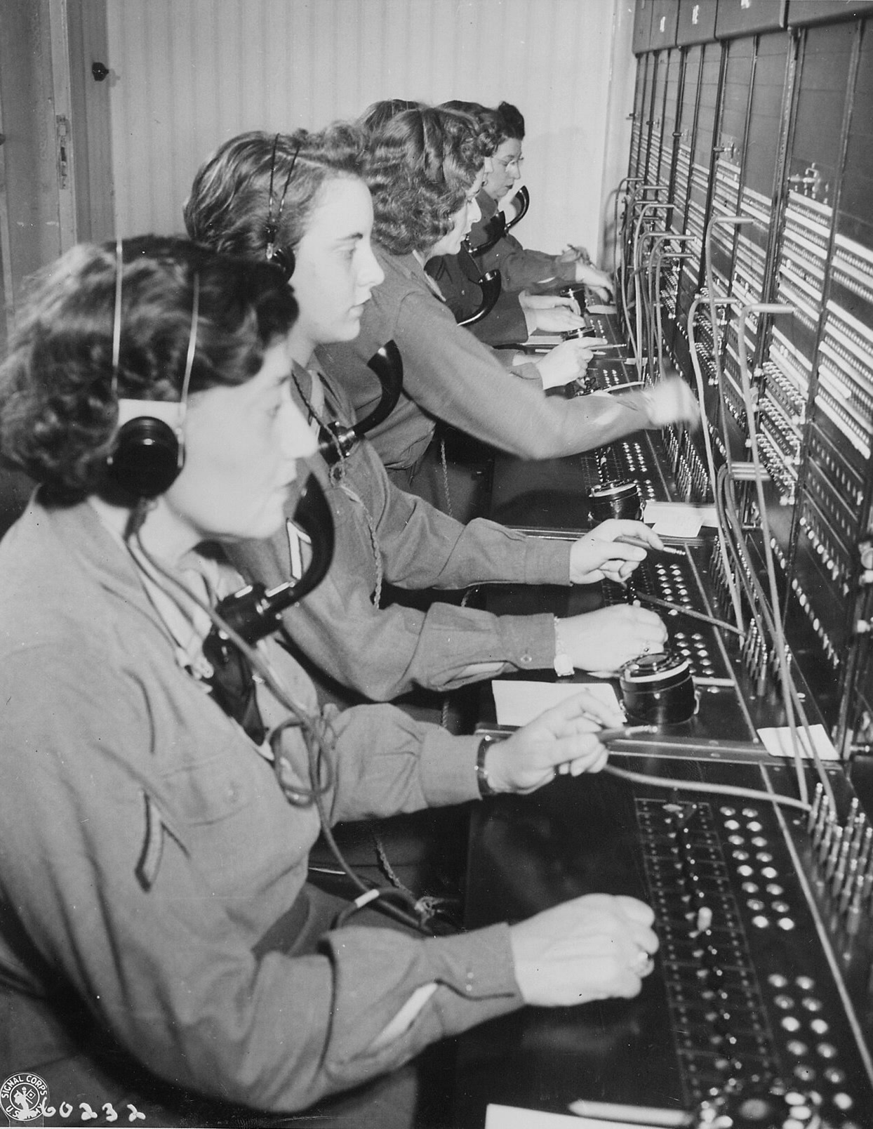 Women's Army Corps operators in headsets work a long switchboard side by side, on the afternoon shift.